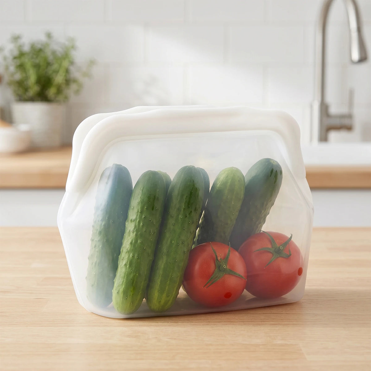 Clear silicone storage bag filled with fresh green cucumbers and red tomatoes on a wooden surface