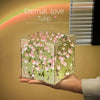 A clear cube night light featuring pink tulips and green foliage, displayed in a hand.