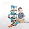 A young boy is sitting next to a multi-level race car track set with a parking garage and various cars.