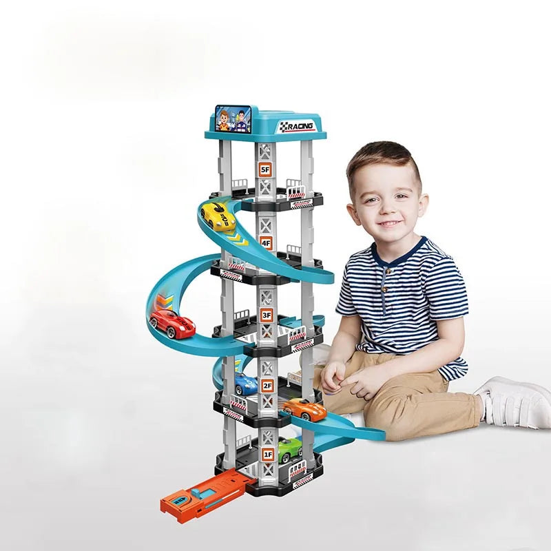 A young boy is sitting next to a multi-level race car track set with a parking garage and various cars.