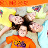 Five children lying on sand smiling while wearing colorful t-shirts