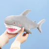A hand holds a gray plush toy of a killer whale and great white shark stuffed animals against a light blue background.