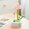 A pink rose flower building block bouquet set with green stems and leaves on a white base.