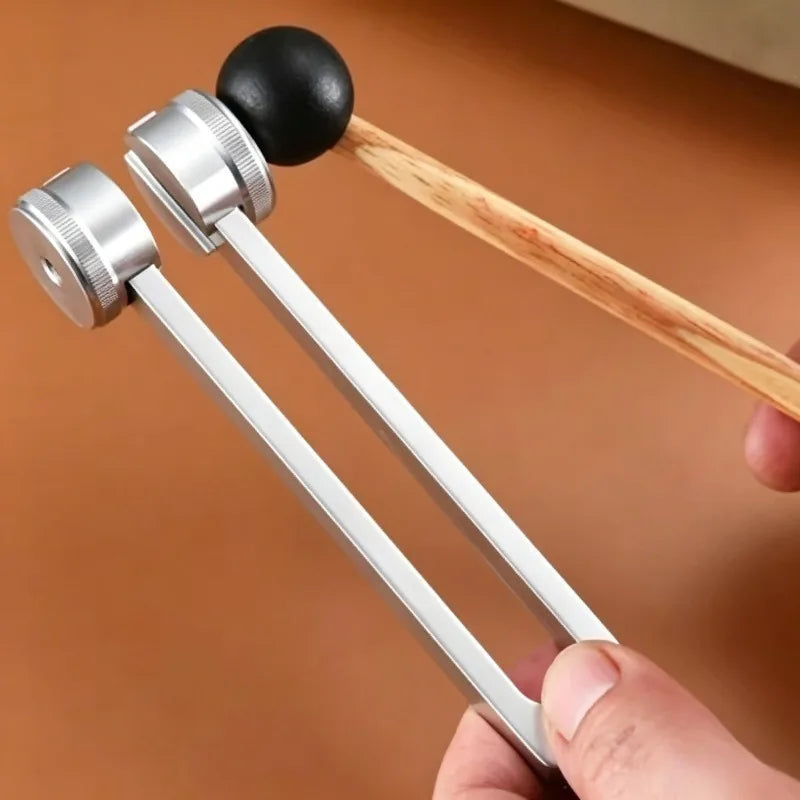 A set of metal tuning forks with wooden handles is held by a hand, used for sound healing and meditation.