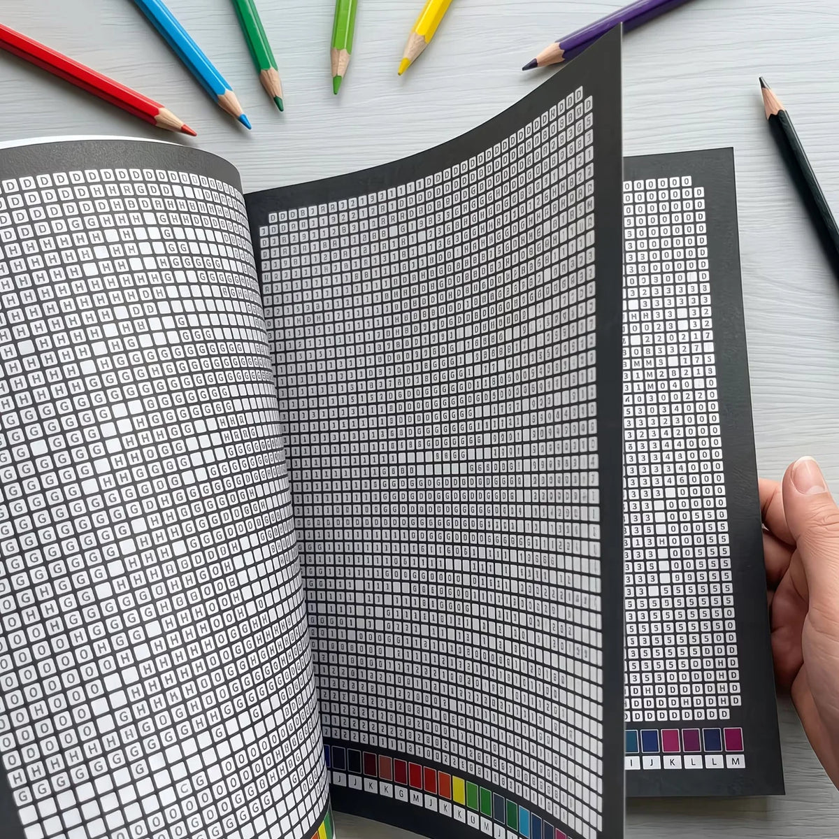 A close-up view of a book with a black and white grid pattern, showing various colors used for a mosaic art project.