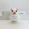 A white crochet pig ornament with pink ears and snout, sitting on a white surface.