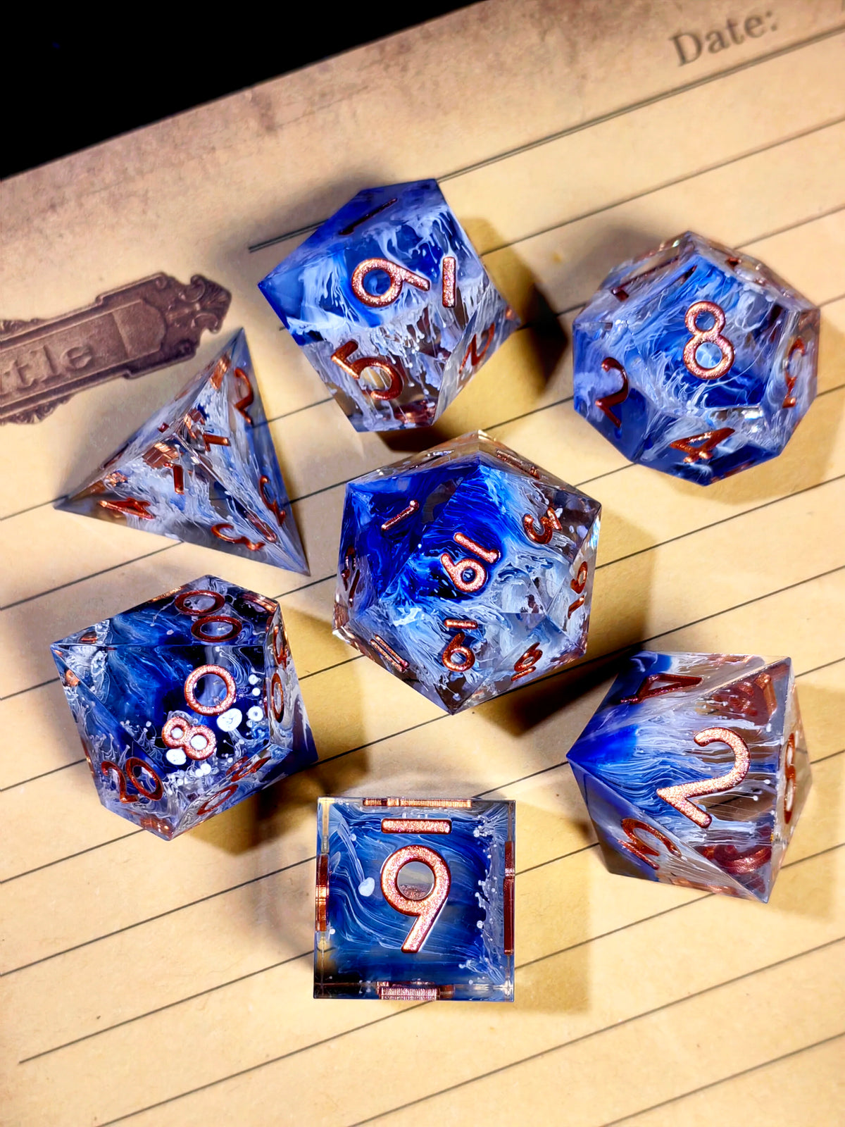 A collection of handcrafted resin polyhedral dice in light purple with gold numbers scattered on lined paper.