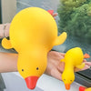 A bright yellow squishy duck fidget toy is held in a person's hand against a blurred outdoor background.