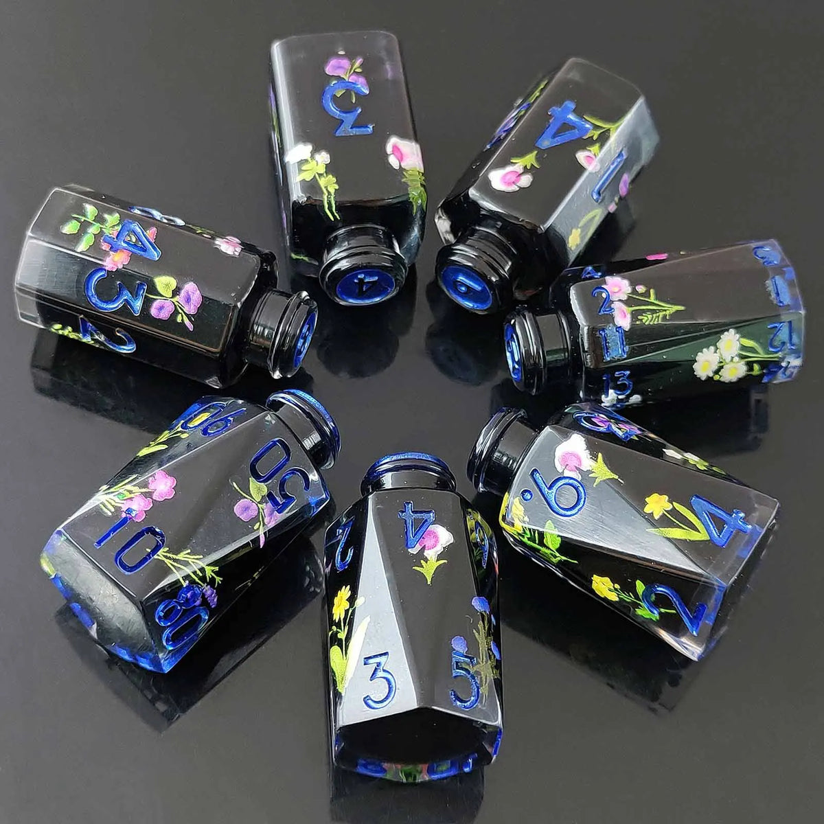 A set of seven floral resin potion bottles shaped like polyhedral dice, featuring various numbers and flowers.