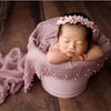 A newborn baby is sleeping inside a pink knit wrap with a floral pearl headband.