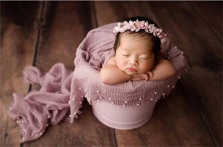 A newborn baby is sleeping inside a pink knit wrap with a floral pearl headband.