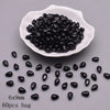 A white dish holds numerous black water drop Czech glass beads for jewelry making.