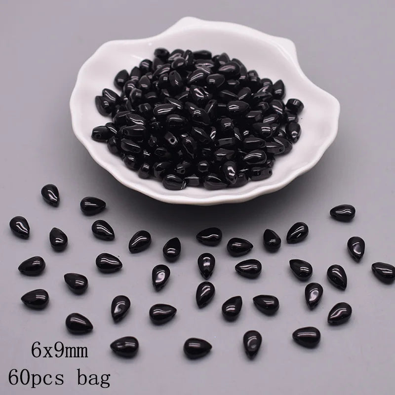 A white dish holds numerous black water drop Czech glass beads for jewelry making.