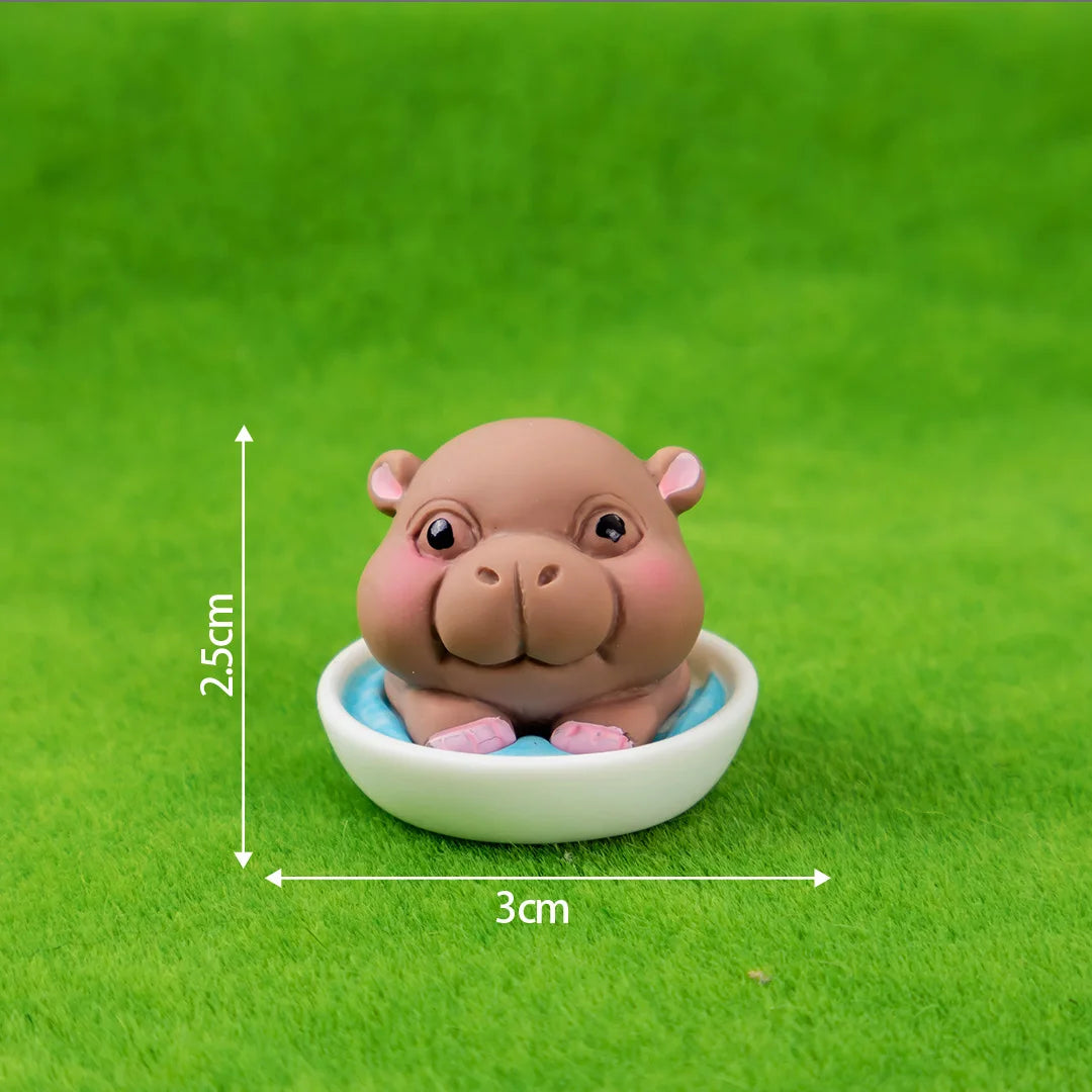 A small, light brown resin hippo figurine sitting in a white bowl on green grass.