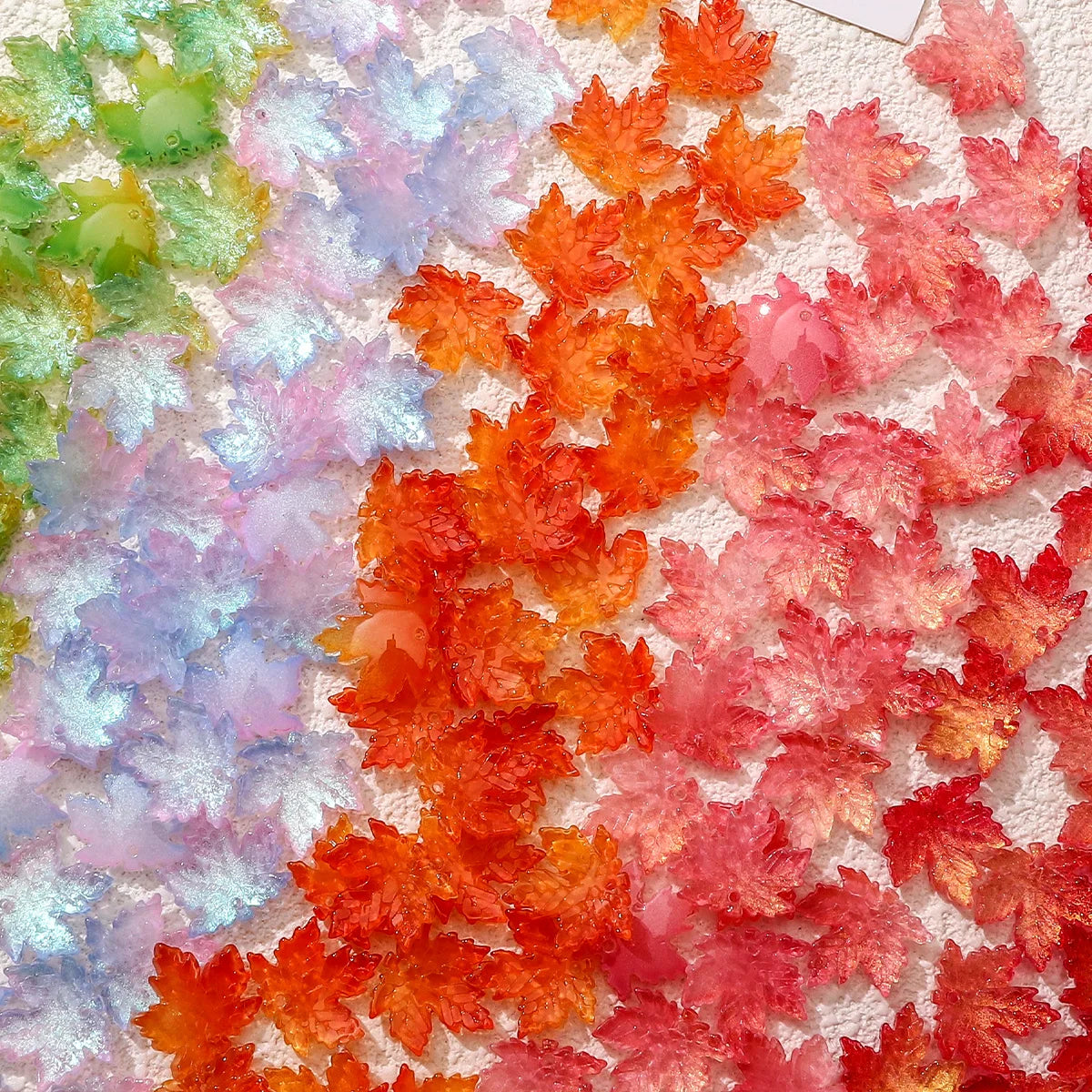 A close-up of colorful maple leaf glass beads in shades of green, purple, orange, and red.