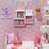 A pink and white themed display featuring a kitten miniature dollhouse puzzle kit with furniture and decorative elements.