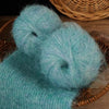 A close-up of two fluffy, light blue alpaca blend yarn balls resting on a woven basket.