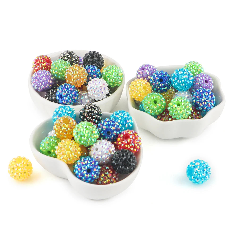 A collection of colorful rhinestone resin bayberry ball beads in various shades and sizes displayed in white bowls.