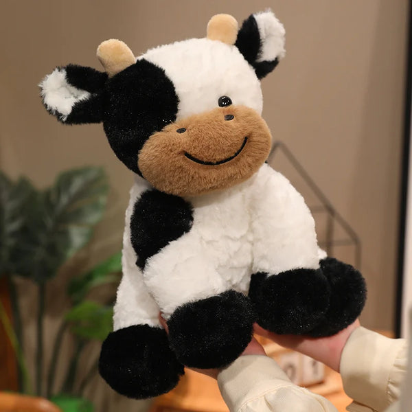 A white and black plush cow stuffed animal toy being held by a person.