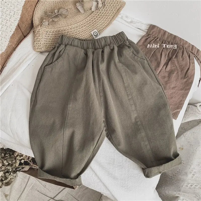 Olive green loose wide-leg harem pants for boys laid out on a white surface with a beige hat.