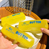 Three yellow butter squishy toys are displayed on a white plate with a wire cage in the background.