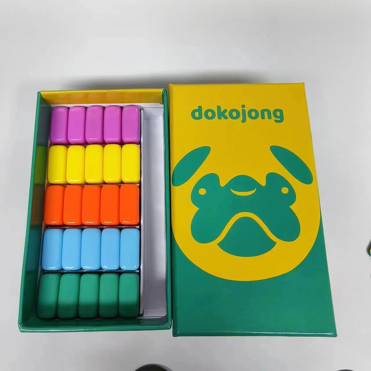 A collection of colorful dice in various shades of pink, yellow, and blue packaged in a green box.