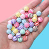 A hand holds a collection of colorful polymer clay marshmallow charms in various stripes and solid colors.