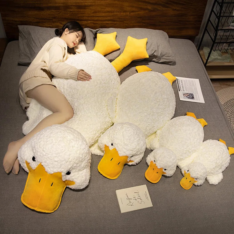 A woman is relaxing on a couch surrounded by several giant white plush duck pillows.