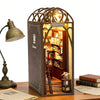 A wooden miniature dollhouse kit displayed in a decorative, arched display box with internal shelving and lighting.