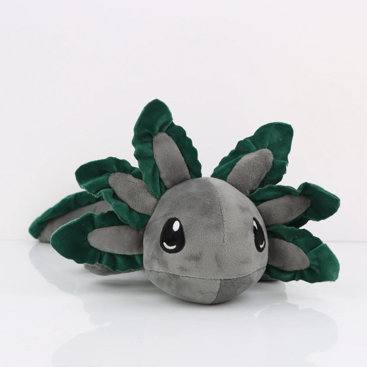 A soft gray and green plush toy of an axolotl with large eyes and leafy appendages.