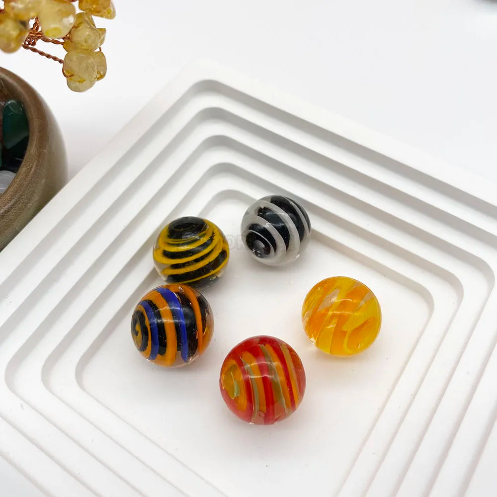 Collection de billes en verre colorées, jaune, noire et blanche, et orange, arrangées sur un plateau blanc.