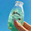 A hand holds a clear bottle containing a green liquid and a small, squishy toy labeled Chiboki.