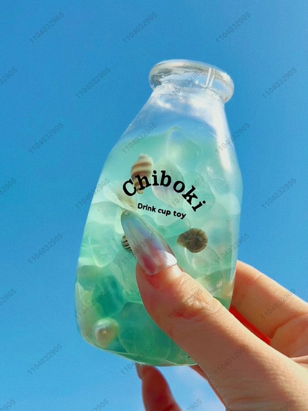 A hand holds a clear bottle containing a green liquid and a small, squishy toy labeled Chiboki.