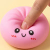 A hand is squeezing a pink, face-shaped squishy stress relief toy with black eyes and red cheeks.