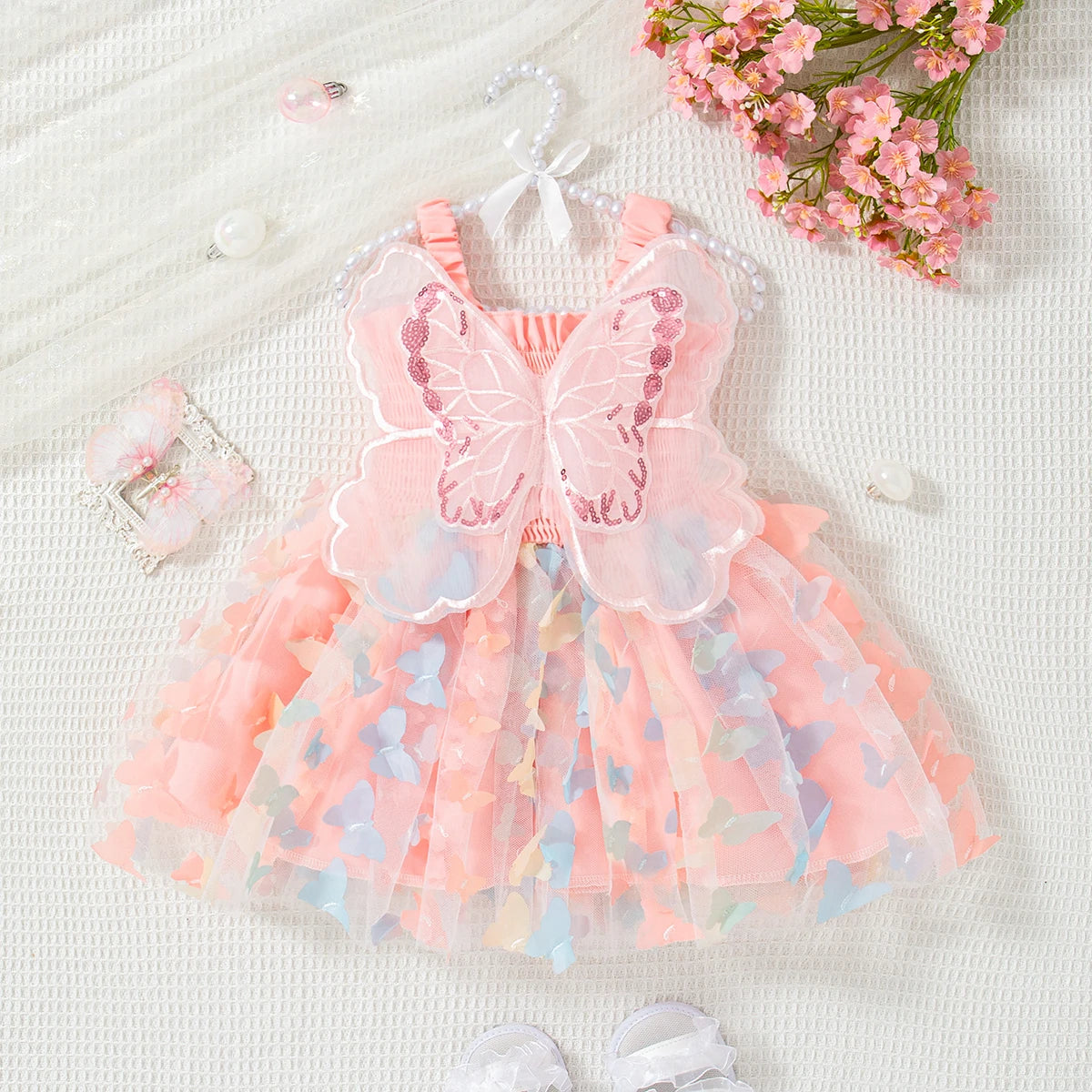 A pink butterfly-style dress for a baby girl with sheer fabric and floral accents, laid on a white surface.
