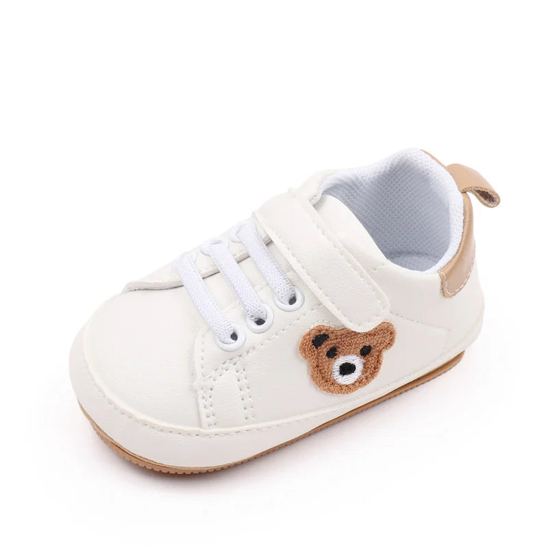 A pair of light beige baby sneakers featuring a cute brown bear face design.