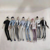 A line of diverse poseable plush dolls dressed in various styles and colors standing against a white background.