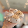 A pair of beige soft sole first walker shoes shaped like bears, held in a hand.
