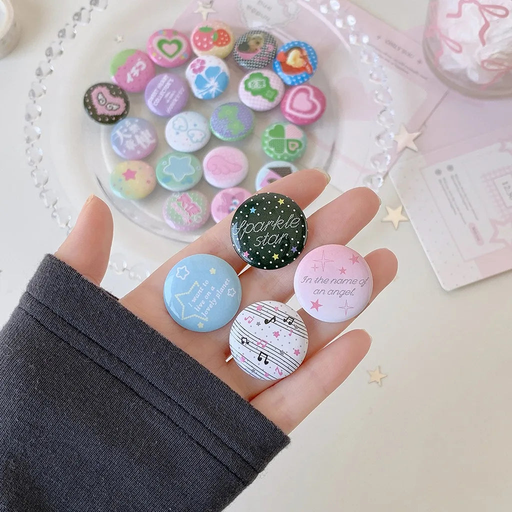 A hand holds a collection of colorful kawaii mini pin badges on a white plate and pink paper.