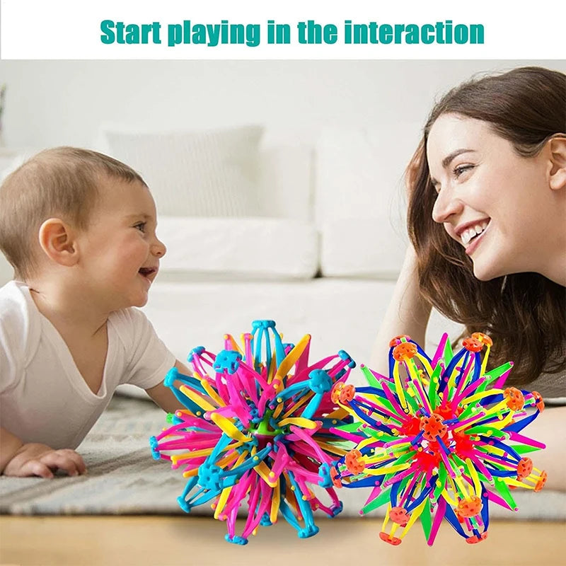 A smiling woman interacts with a baby while playing with a colorful expandable magic ball toy.