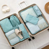 A set of light blue and beige travel packing cubes and storage bags organized in a cardboard box.