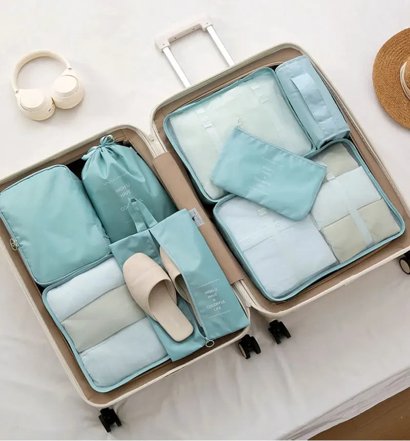 A set of light blue and beige travel packing cubes and storage bags organized in a cardboard box.