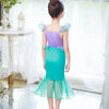 A girl models a purple and teal mermaid fantasy dress with ruffled fishtail skirt against a bright window background.