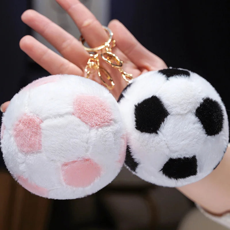 A hand holds a white and pink plush soccer ball toy against a dark background.