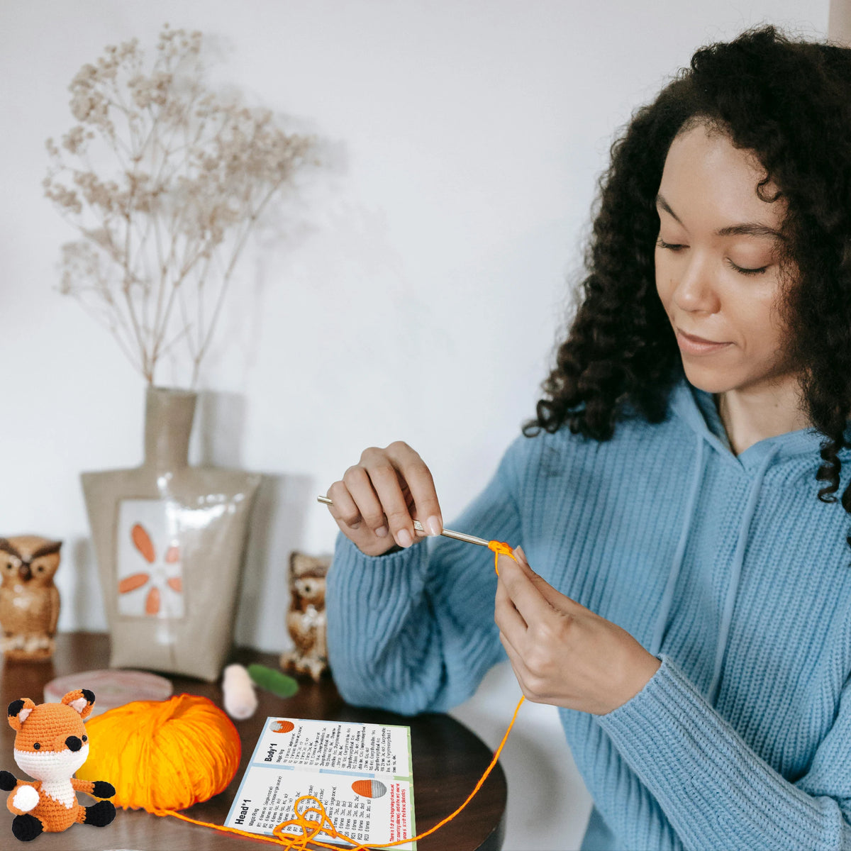 A person is using a beginner crochet kit with a little fox design to create a piece of orange yarn.