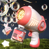 A pink automatic bubble machine with lights is shown next to liquid soap and floating bubbles on green grass.