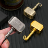 A hand holds a silver hammer-shaped metal fidget spinner with a gold handle and a brass-colored component on a dark surface.
