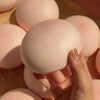 A hand is holding a pink, egg-shaped squishy stress relief toy with a slightly textured surface.