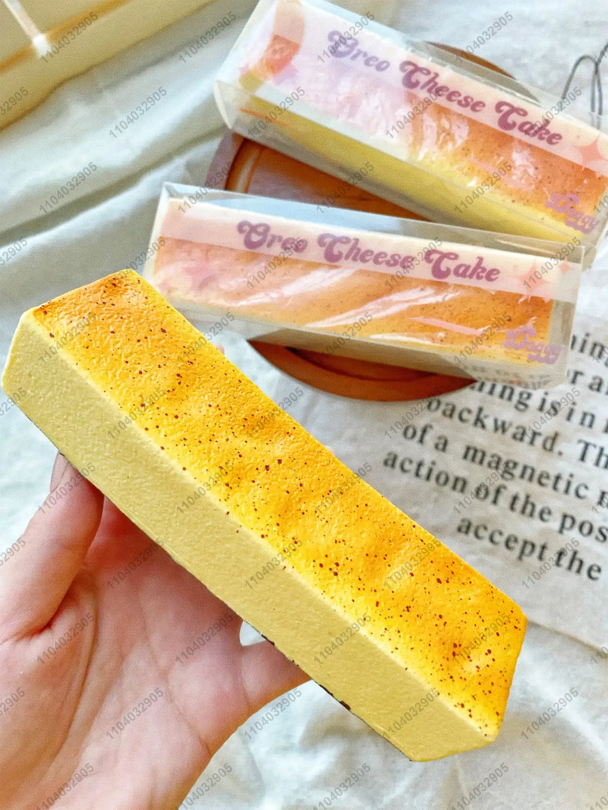 A yellow butter stick squishy toy is held in a hand, next to a packaged cheese cake product.