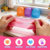 Hands hold a pink squishy stress ball next to colorful foam balls on a windowsill.